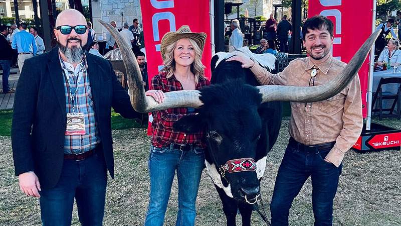 Three employees posing with a longhorn at an outdoor event