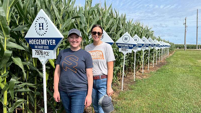 Two employees standing in a corn test plot field