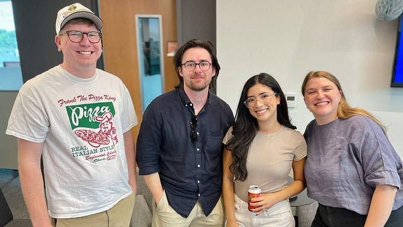 Four employees smiling together in an office common area