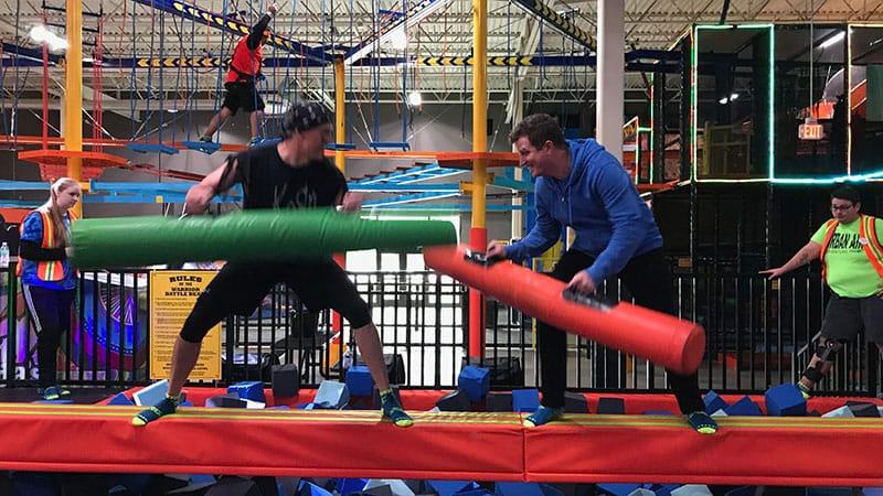 2 people playing american gladiators and knocking each other off a platform