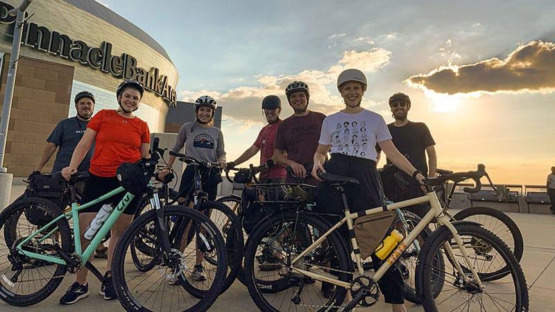 Employees posing with their bikes in front of Pinnacle Bank Arena