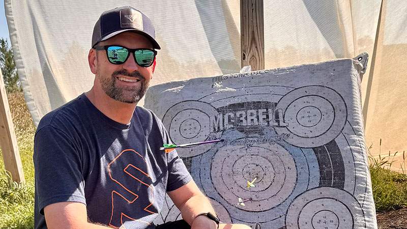 An employee smiling beside an archery target after practice shots