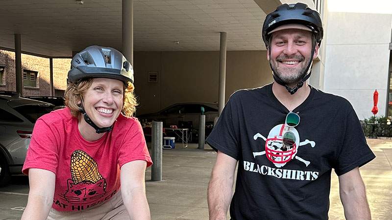 Two employees smiling while wearing bike helmets