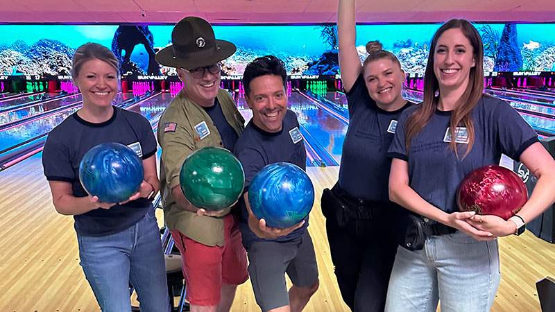 Five employees holding bowling balls and celebrating on the lanes