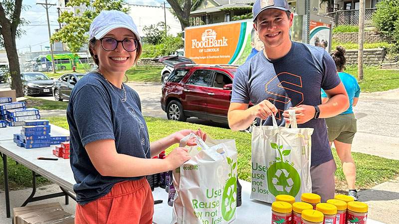 Two employees volunteering at a food bank distribution table