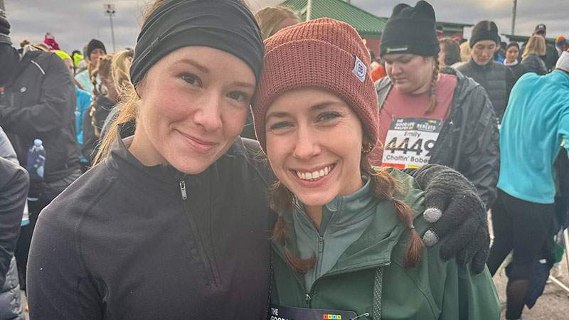 Two employees smiling together in a crowd of runners before a race
