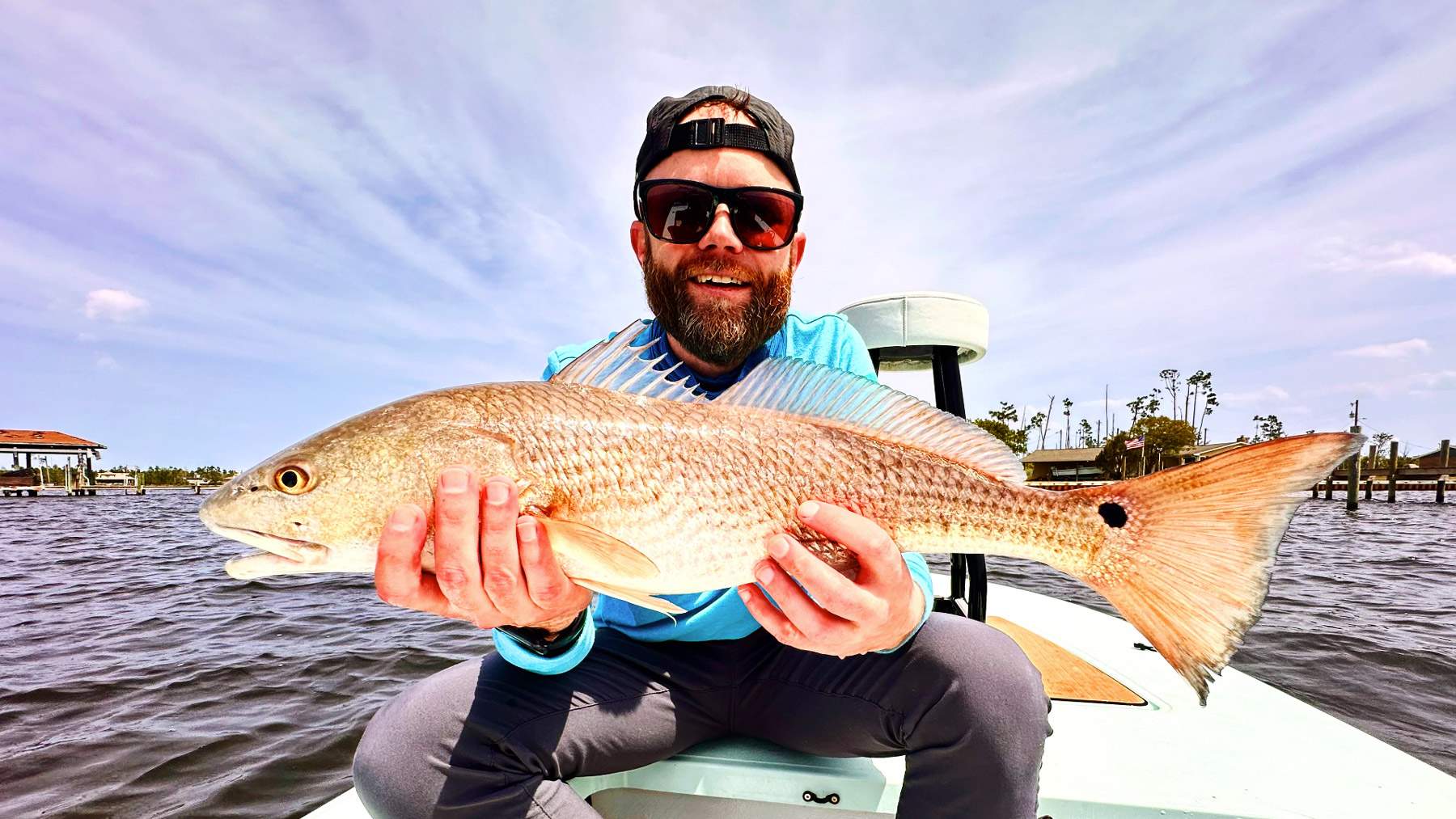 Man sitting on a boat holding a freshly caught fish.