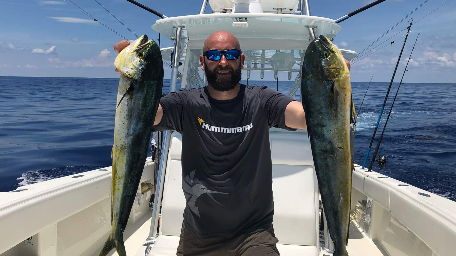 Man on a boat holding two freshly caught fish.
