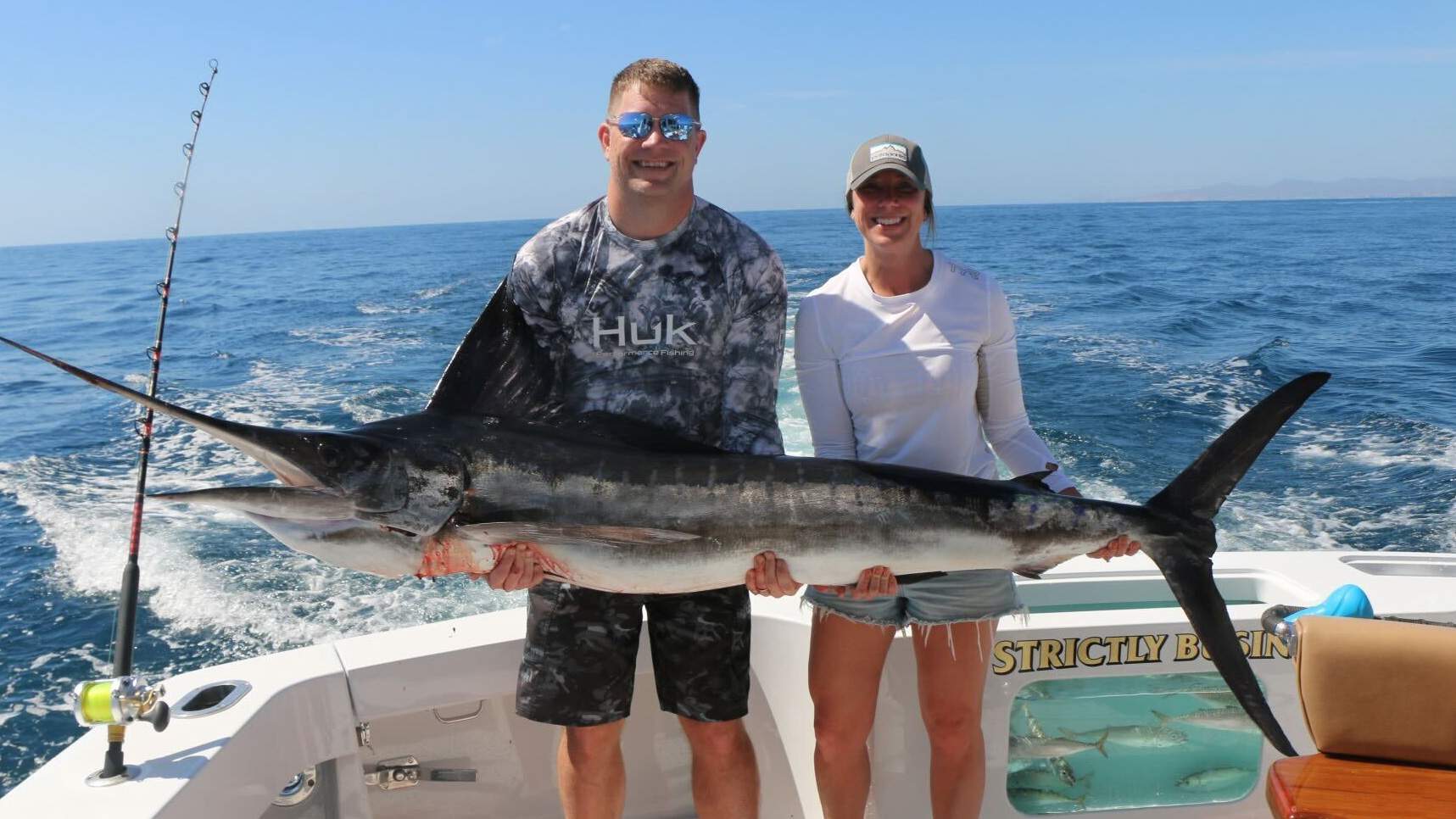 Two people on a boat holding a freshly caught fish.