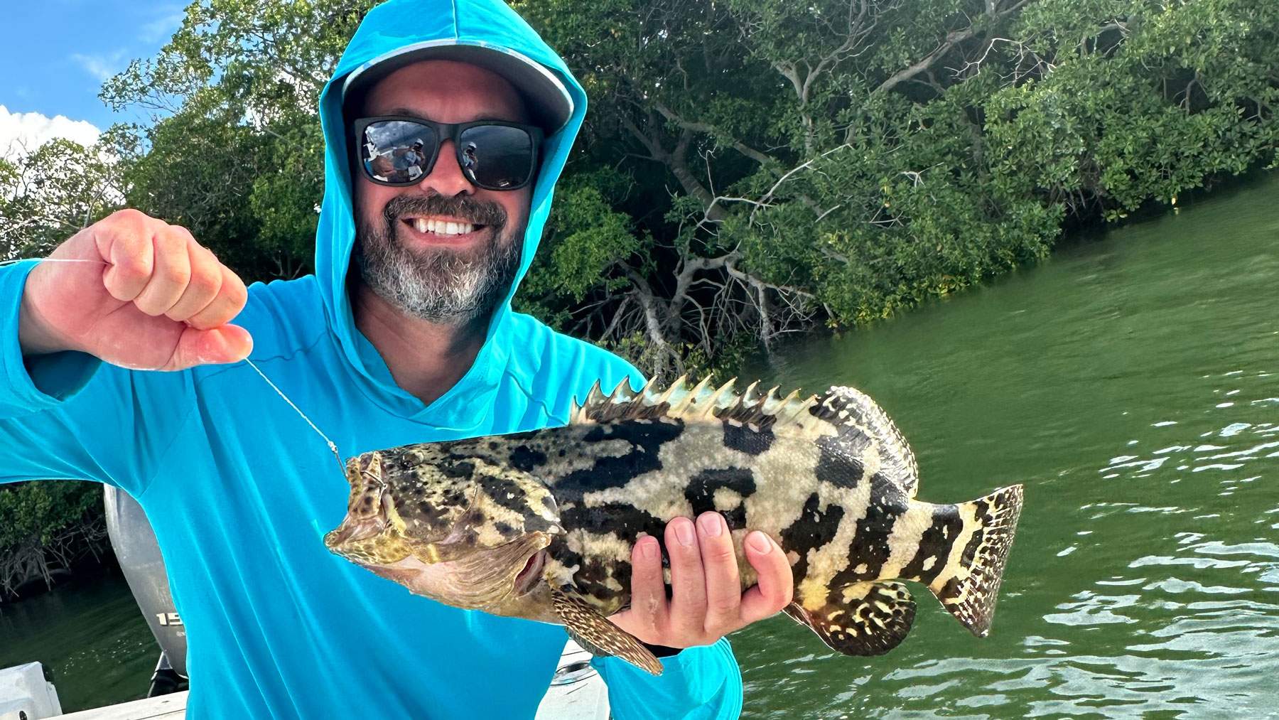 Man on a boat holding a freshly caught fish.